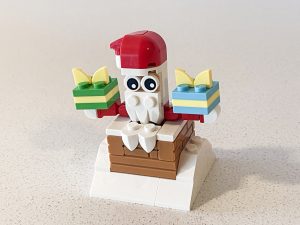 A little lego build of santa sticking out of the chimney holding two presents.